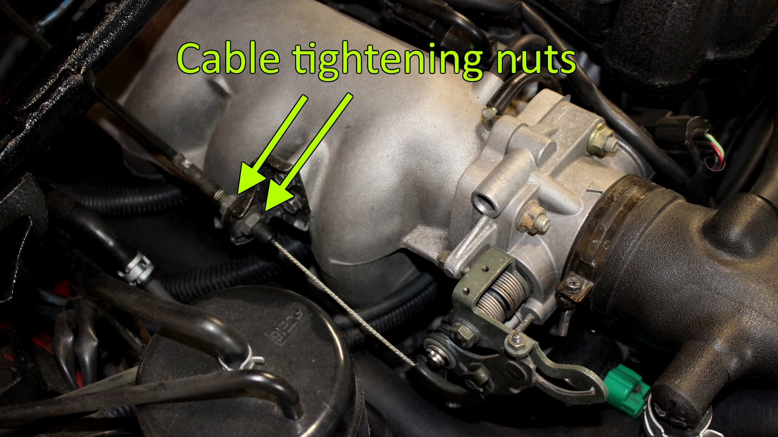 Miata accelerator cable mounted to intake manifold bracket and connected to throttle body with tightening nuts labeled